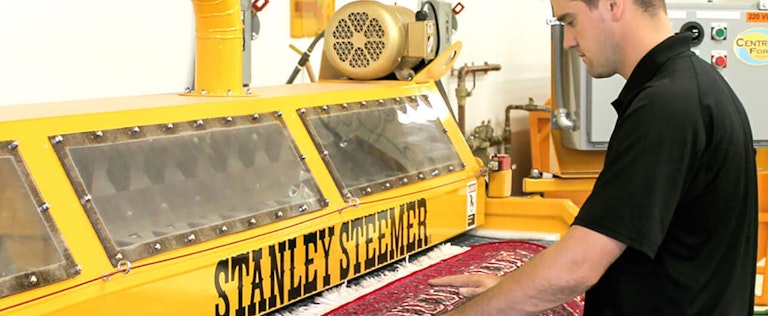 Stanley Steemer employee preparing to feed a rug to a steam cleaner machine